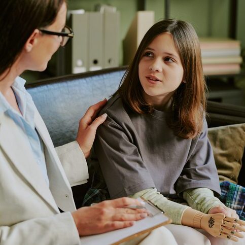 Teenage girl with prosthetic limb engaging with therapist on sofa focusing on recovery and future steps Together discussing personal progress in friendly environment